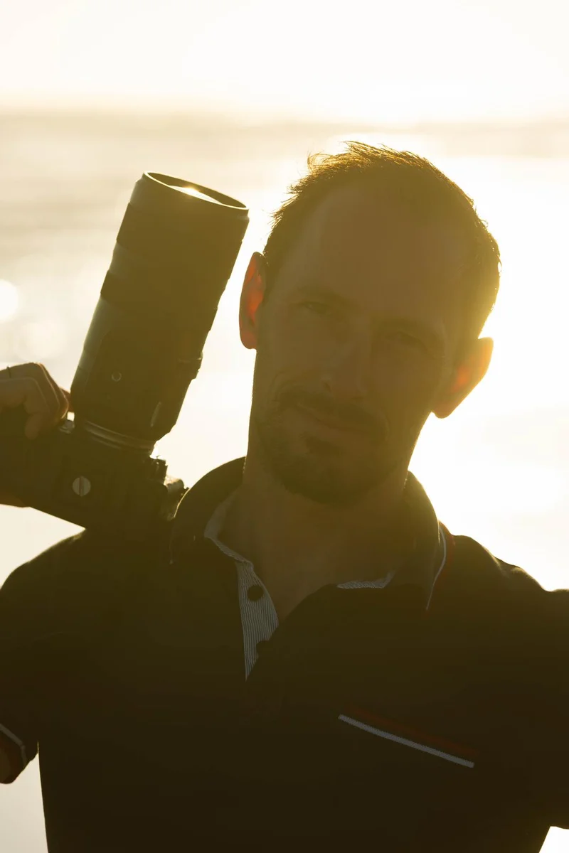 Aurélien Lambert, photographe, appareil photo à l'épaule, éclairé en contre-jour par la lumière dorée du soleil