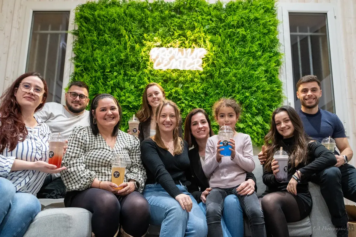Groupe de sept personnes souriantes assises devant un mur végétal, tenant des boissons lors d'un événement