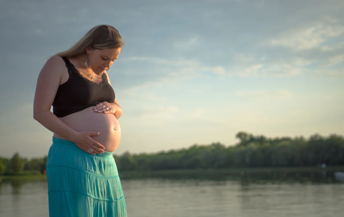 Séance maternité, femme enceinte au bord d'un lac au coucher du soleil