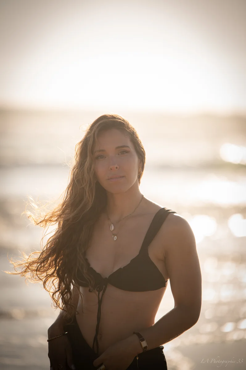 Portrait d'une femme aux cheveux longs au vent, éclairée par la lumière dorée du coucher de soleil en bord de mer